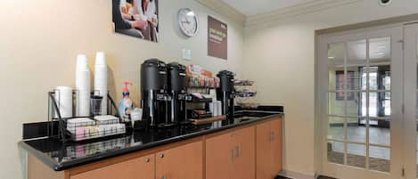 A breakfast bar with coffee makers, cups, and condiments.