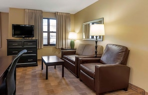 Une chambre d’hôtel équipée d’un téléviseur à écran plat, d’un canapé, d’une table basse, d’une lampe et d’une fenêtre avec des rideaux.