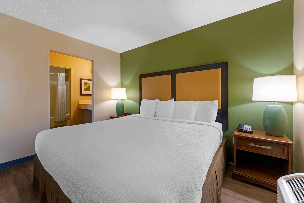 A hotel room with a large bed, two bedside tables with lamps, a nightstand, and a chair.
