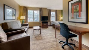 Habitación de hotel con sofá, escritorio, televisor y un cuadro en la pared.