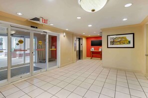 A hotel lobby with an exit sign, automatic caution signs, a tiled floor, and a framed picture on the wall. - Extended Stay America Suites Orlando Conv Ctr 6443 Westwood (Orlando)