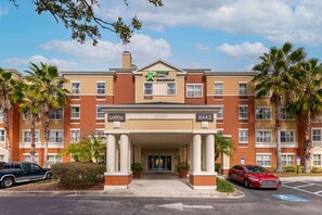 Un hotel Stay America con entrada al vestíbulo, palmeras y zona de estacionamiento.
