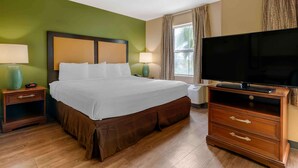 Una habitación de hotel con una cama grande, dos mesitas de noche con lámparas, un televisor sobre un mueble de madera y una ventana con cortinas.