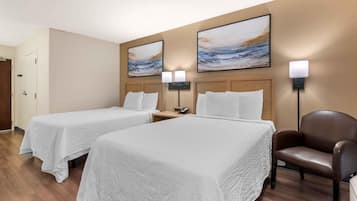 A hotel room with two beds, a chair, and artwork on the walls.