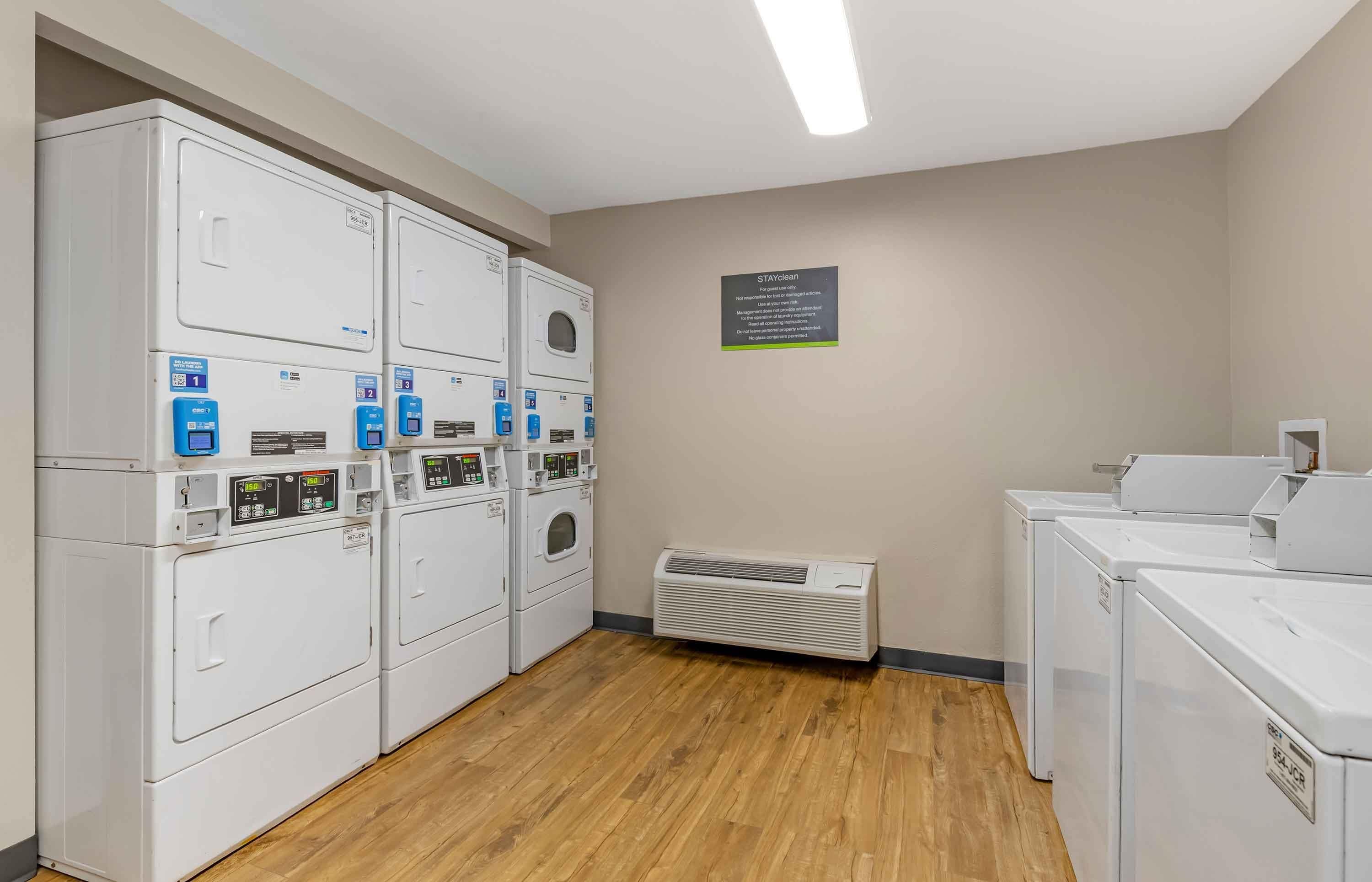 A laundry facility with multiple washing machines and dryers, a sign with instructions, and a ventilation unit.