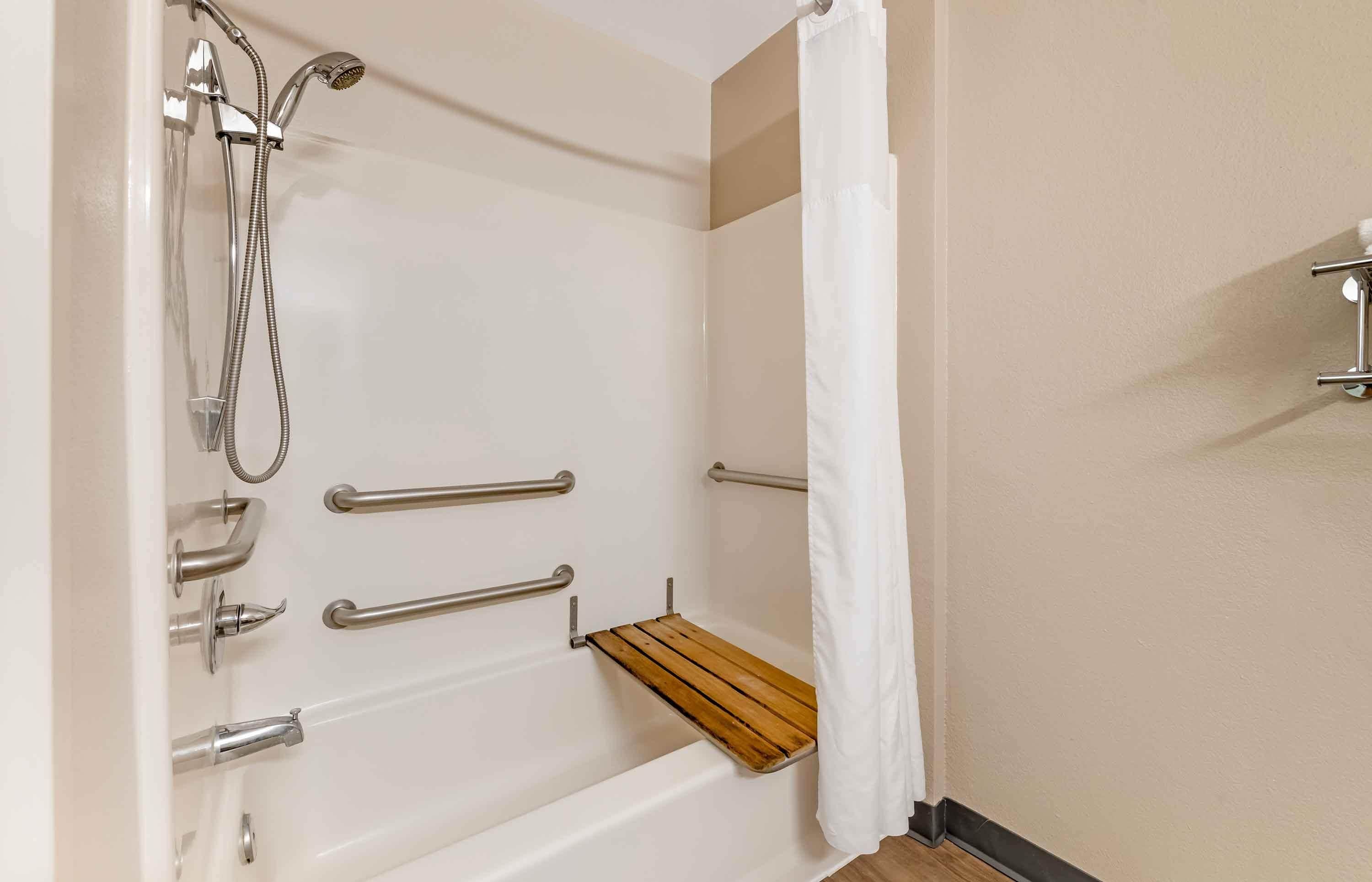 Ein Badezimmer mit Dusche, Haltegriffen und einem Holzregal.