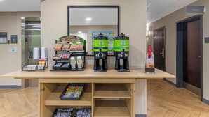 Zona de recepción de un hotel con una estación de café, un cesto de basura y un letrero en el suelo que indica el primer piso.