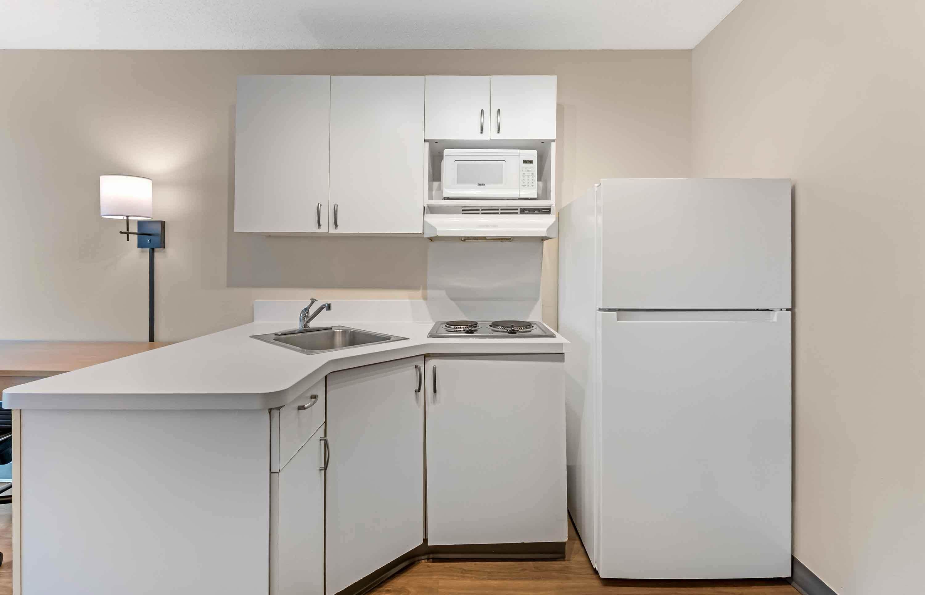 A compact kitchen with white cabinetry, a microwave, a stove, and a refrigerator.