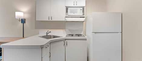 A compact kitchen with white cabinetry, a microwave, a stove, and a refrigerator.