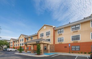 A multi-story hotel with a covered lobby area, parking lot, and a clear blue sky.