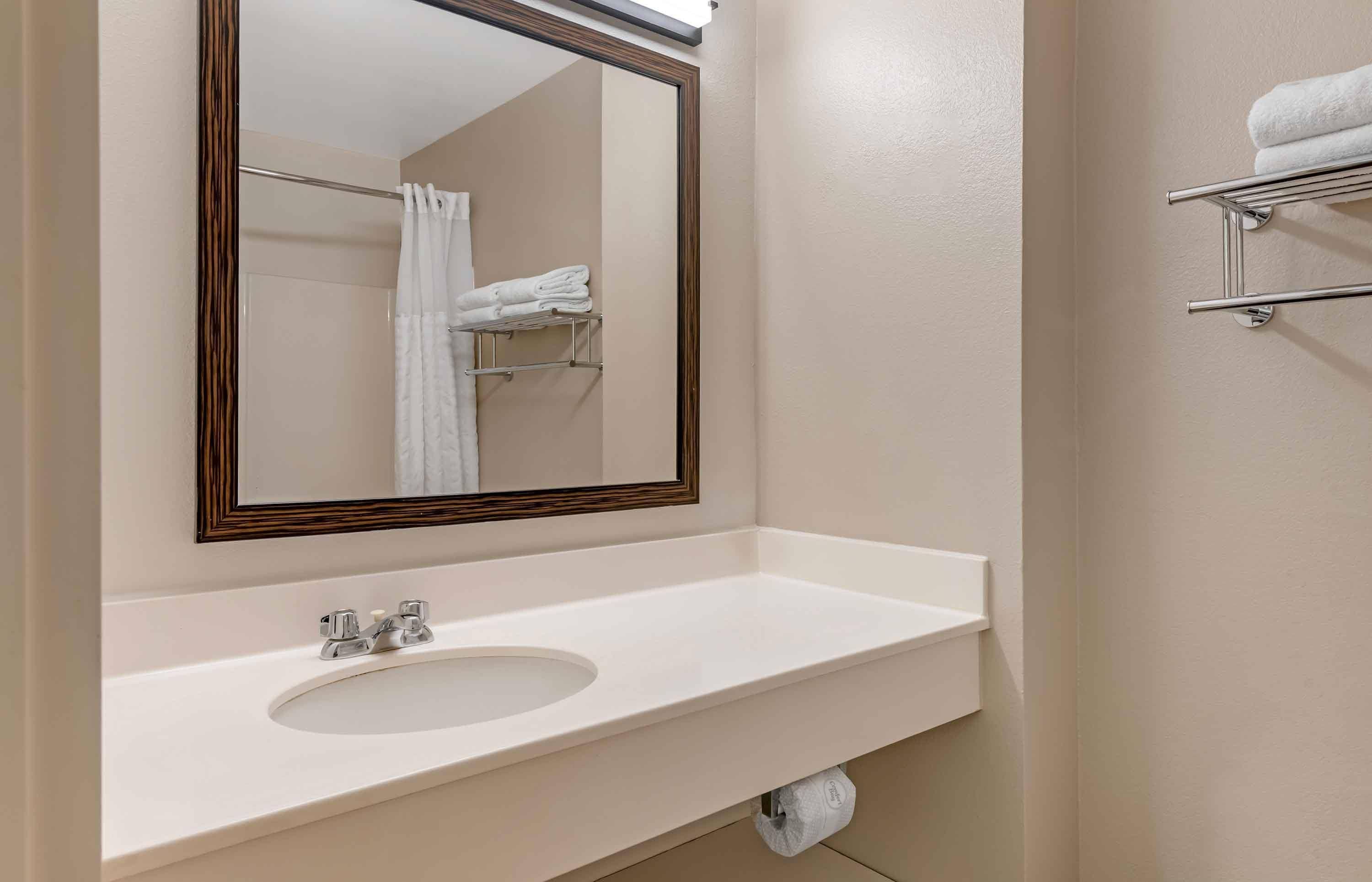 A bathroom with a white sink, a mirror with a wooden frame, and a towel rack with folded towels.