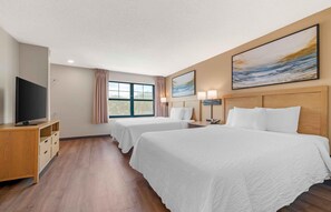 A hotel room with two beds, a television, a window with curtains, and artwork on the walls.