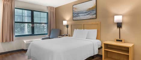 A hotel room with a bed, bedside tables, a chair, a window with curtains, and a painting on the wall.