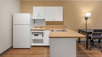 A compact kitchen with white cabinets, a built-in microwave, a sink, and a dining area with a table and chairs.