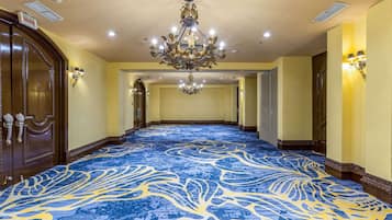 Un corridoio d'hotel con tappeto blu, lampadari e porte in legno.