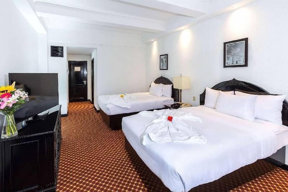 A hotel room with two beds, a desk, a lamp, and a framed picture on the wall.