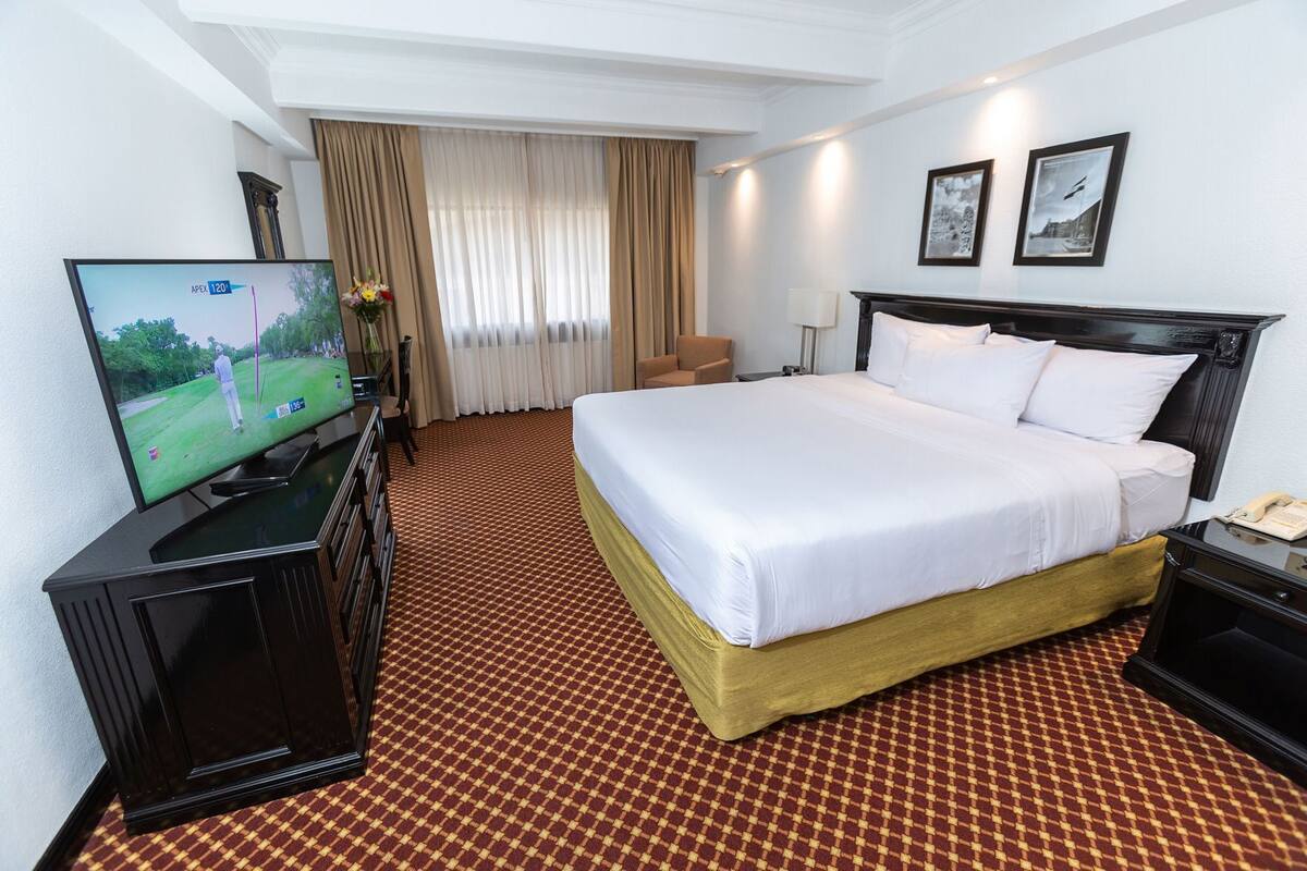A hotel room with a bed, a TV, a desk, a chair, a lamp, and a window with curtains.