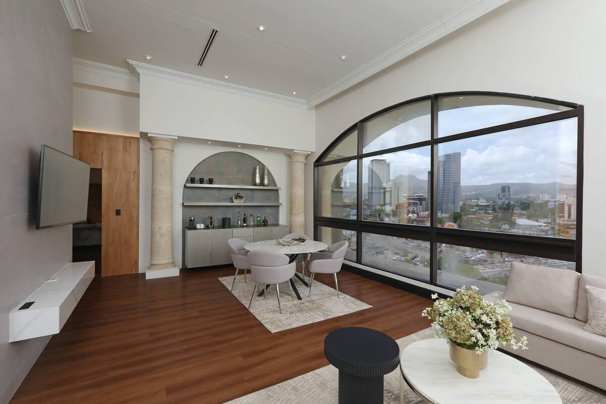 Una sala de estar moderna con comedor, ventanas amplias y vistas a la ciudad, y un televisor de pantalla plana montado en la pared.