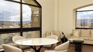 Una sala de estar moderna con una mesa redonda y sillas, un sofá y grandes ventanales con vistas a la ciudad.