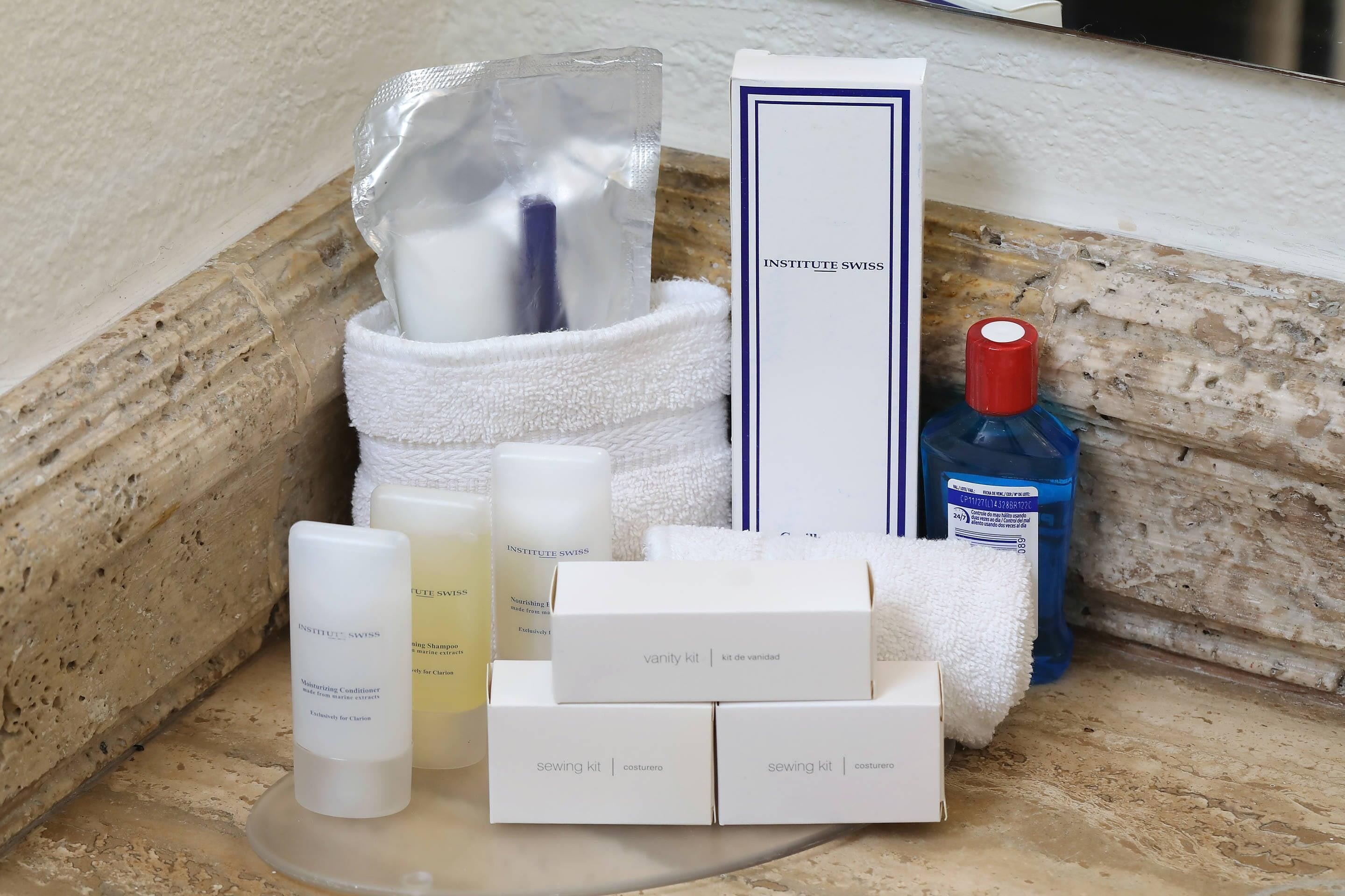 A bathroom vanity with toiletries, including a bottle of blue liquid, a white towel, and a white box labeled "sewing kit."