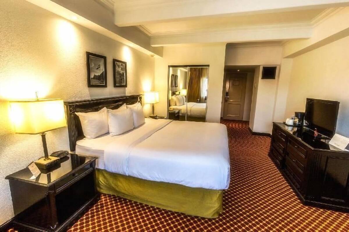 Una habitación de hotel con cama, mesitas de noche, cómoda, televisor y espejo.