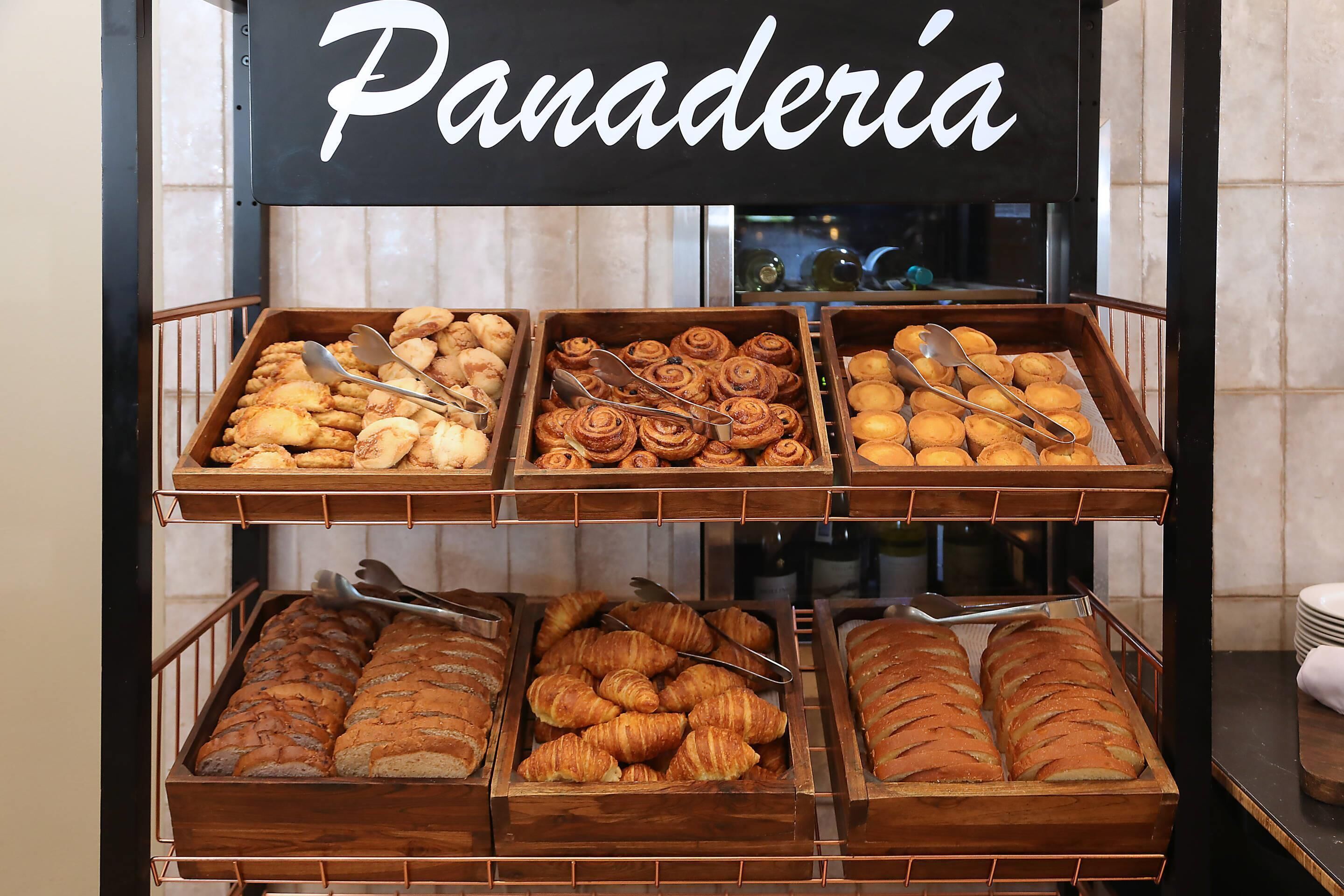A bakery display with various baked goods, including pastries and bread, under a sign that reads 'Panadería.'