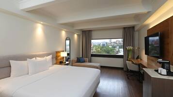 Habitació d'hotel amb un llit gran, escriptori, cadira, televisió i finestra amb vista a la ciutat.