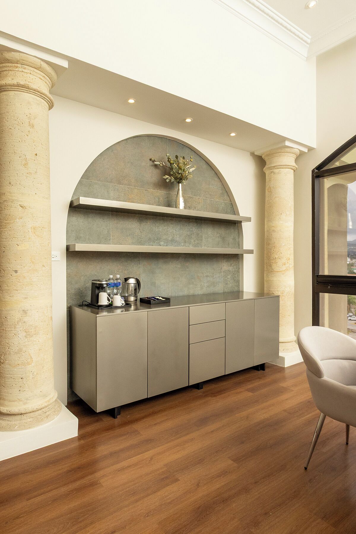 A modern kitchen with a built-in espresso machine, a vase with flowers, and a view through a window.