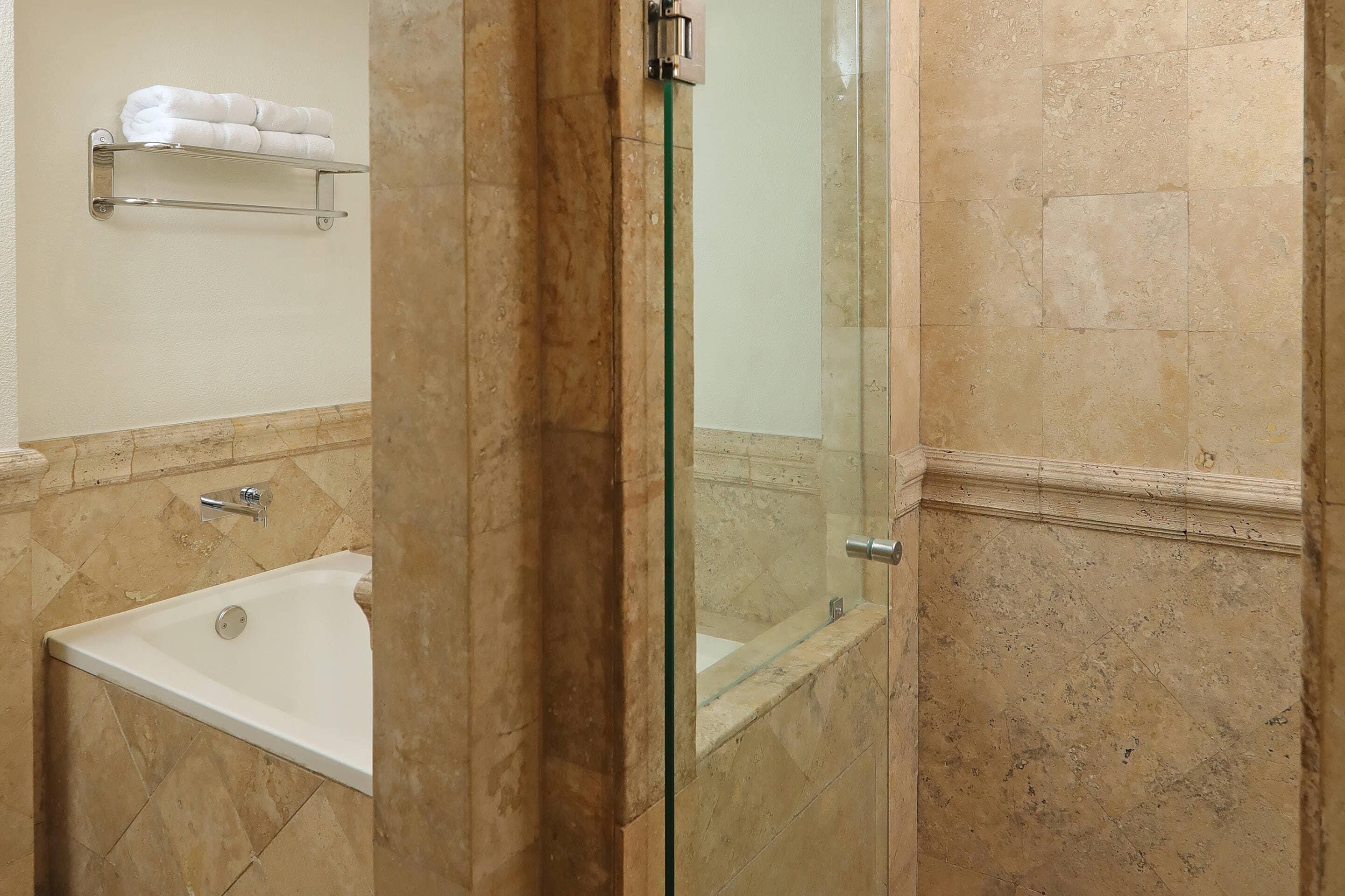 A bathroom with a glass-enclosed shower, a white bathtub, and a towel rack on the wall.