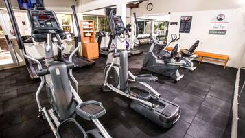 A gym with multiple cardio machines, a weight bench, and a mirror reflecting the equipment.