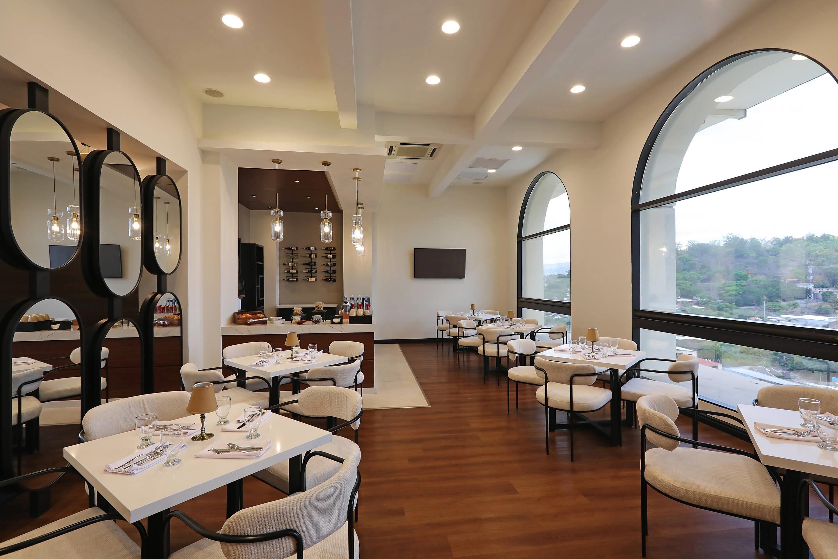A modern dining area with multiple tables and chairs, large mirrors, and a view through large windows.