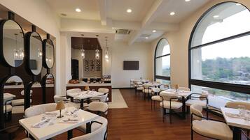A modern dining area with multiple tables and chairs, large mirrors, and a view through large windows.