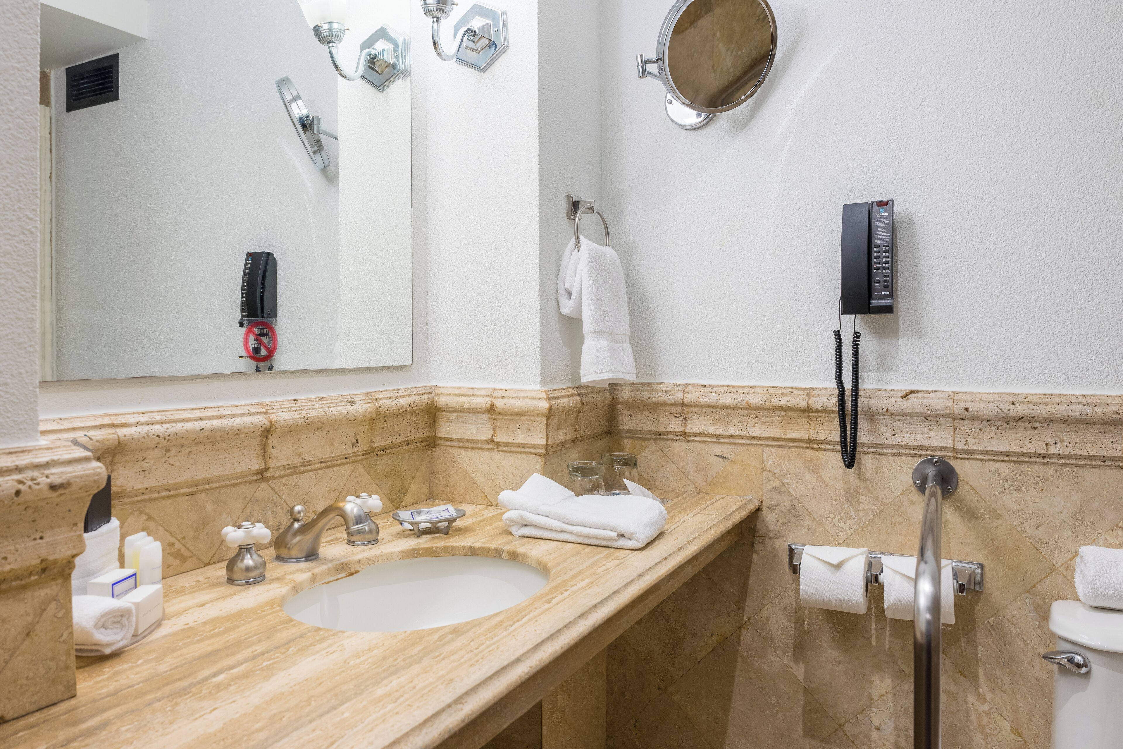 A bathroom with a sink, mirror, towel rack, and a telephone.