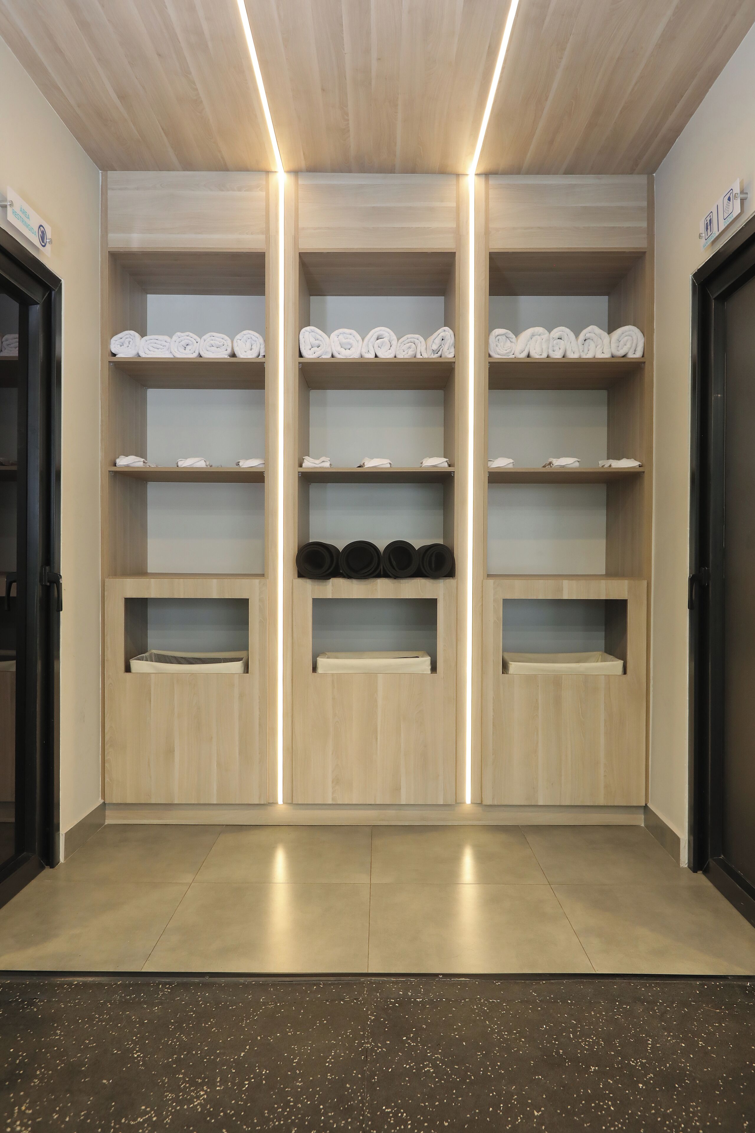 Un interior moderno con estanterías de madera, algunas con toallas enrolladas y otras con sombreros negros.