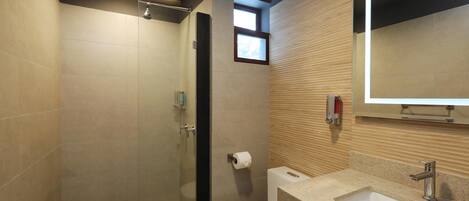 Un baño moderno con ducha envuelta en vidrio, inodoro y lavamanos con espejo.