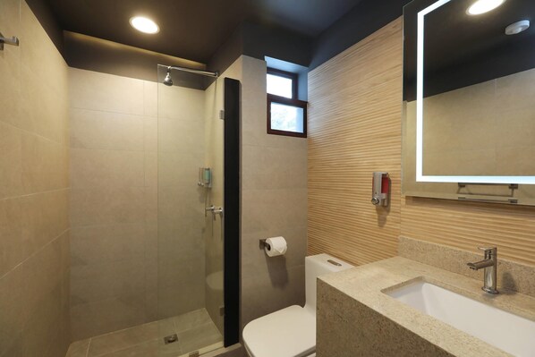 Un baño moderno con ducha envuelta en vidrio, inodoro y lavamanos con espejo.