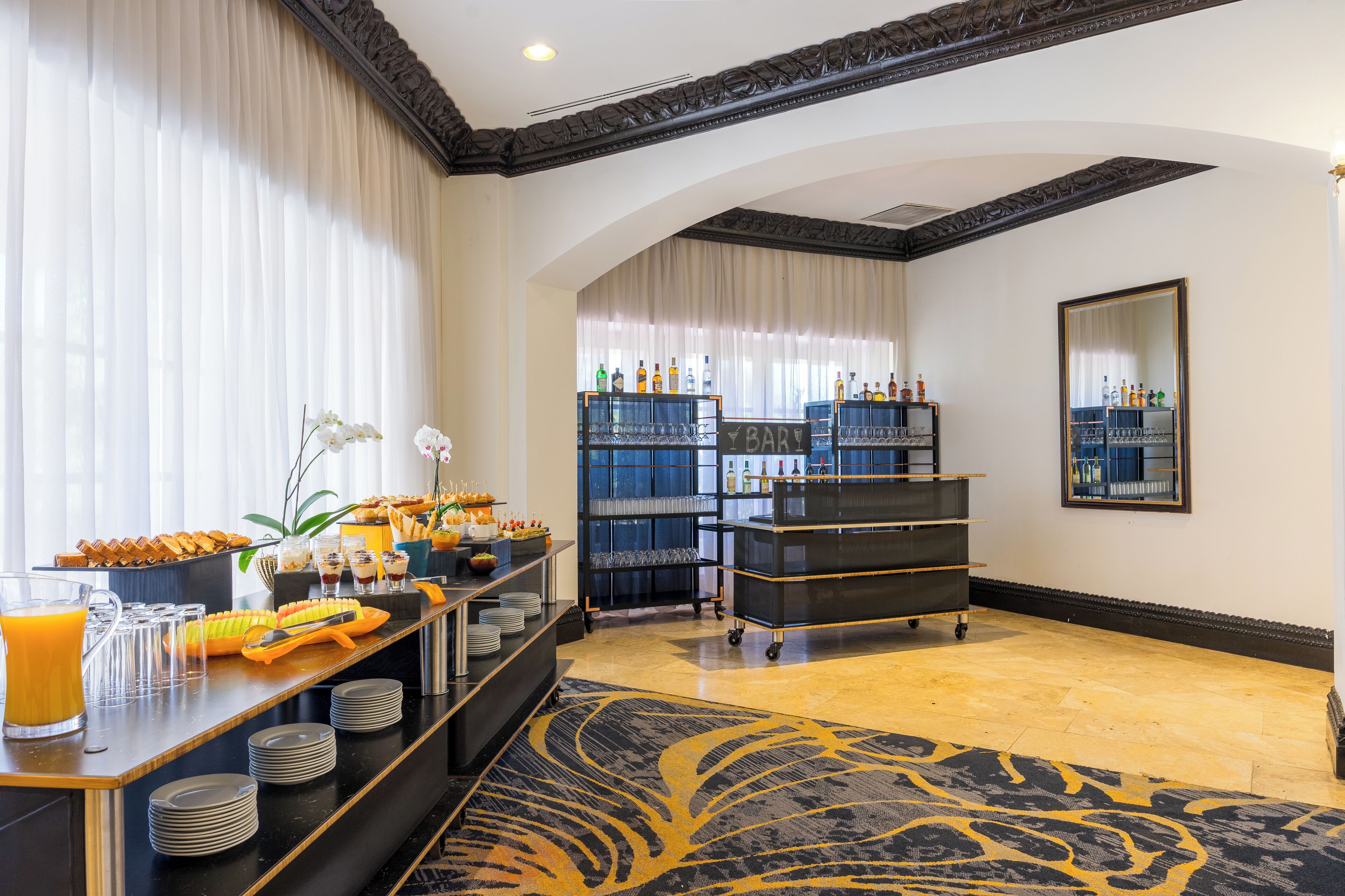 Vestíbulo de hotel con zona de buffet, un bar y un espejo grande en la pared.