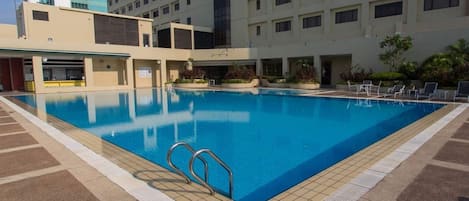 A swimming pool with a tiled deck, surrounded by a building with multiple floors and windows.
