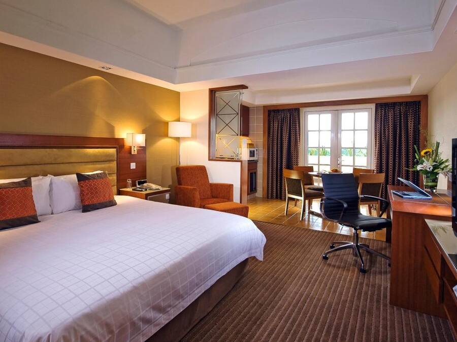 A hotel room with a large bed, a desk with a television, a chair, and a desk lamp.