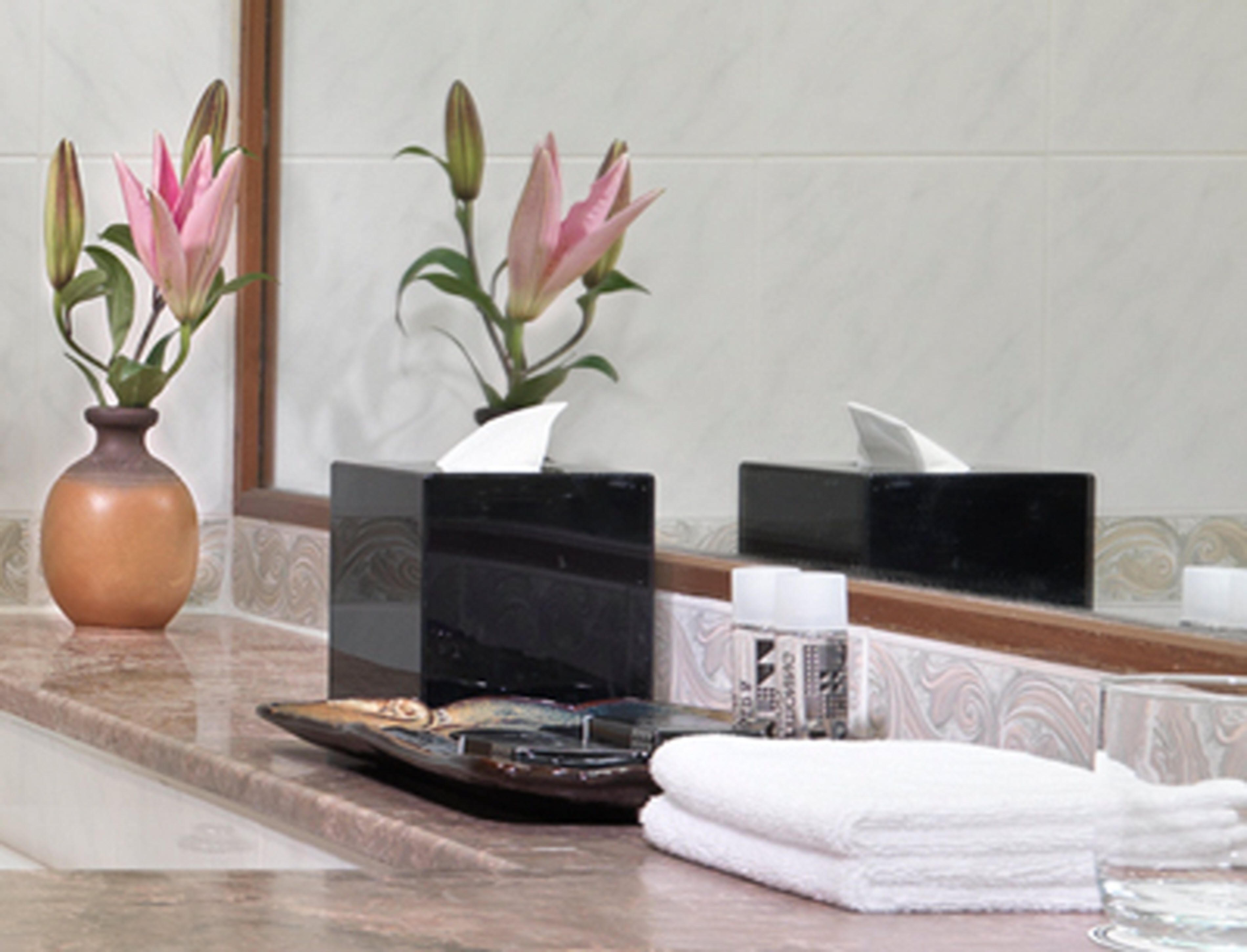 A bathroom vanity with a vase of pink flowers, a tissue box, and a towel.