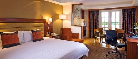 Een hotelkamer met een groot bed, een bureau met een laptop, een stoel en een zithoek met een tafel en stoelen.