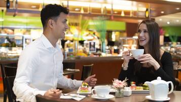 Ein Paar speist in einem modernen Café mit einer Auswahl an Desserts und einer Teekanne auf dem Tisch.