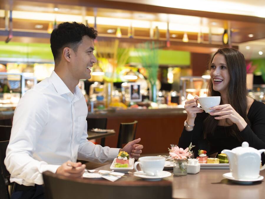 Ein Paar speist in einem modernen Café mit einer Auswahl an Desserts und einer Teekanne auf dem Tisch.