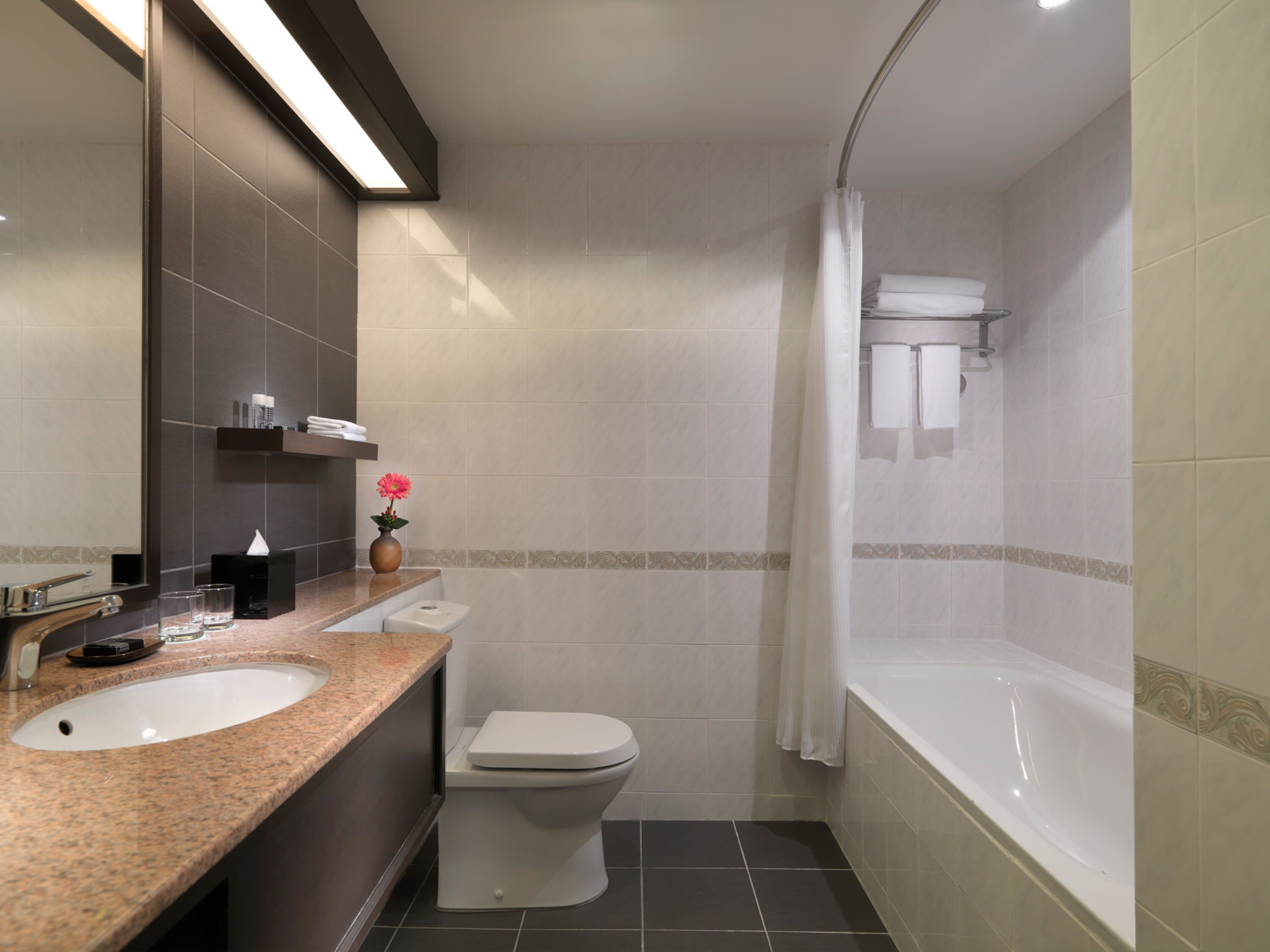 Un baño moderno con encimera de granito, inodoro blanco, bañera y cortina de ducha.