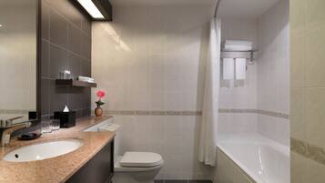 Un baño moderno con encimera de granito, inodoro blanco, bañera y cortina de ducha.