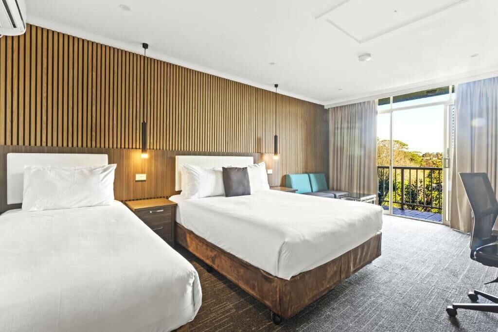 Ein Hotelzimmer mit zwei Betten, einem Balkon und Blick auf Grünflächen.