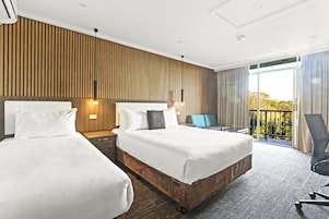 Quarto de hotel com duas camas, varanda e vista para o verde.