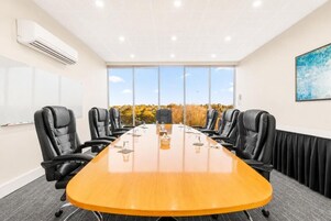 Un salón de conferencias con una larga mesa, sillas negras y vistas a árboles a través de amplios ventanales.