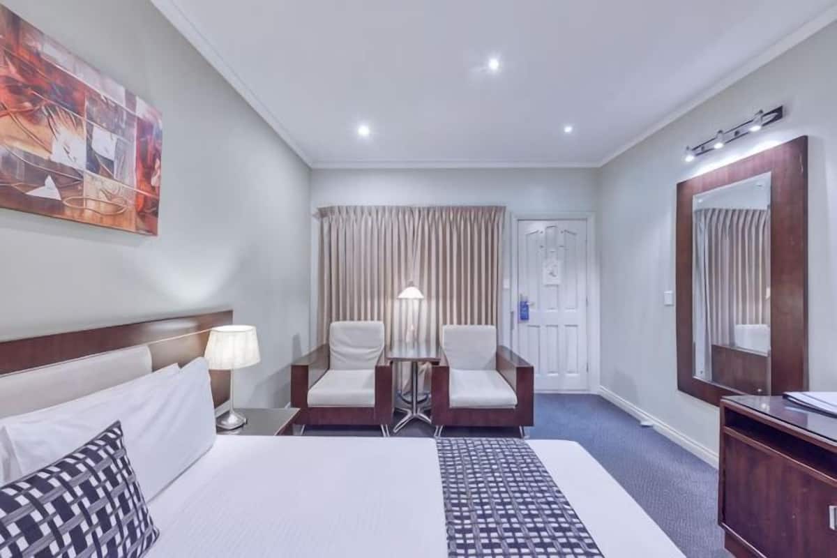 Una habitación de hotel con cama, dos sillas, escritorio, lámpara, espejo y puerta.