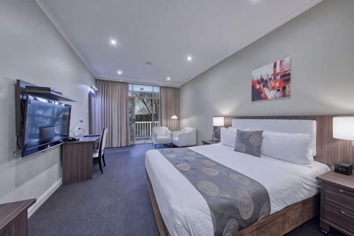 Habitación de hotel con una cama grande, un escritorio, televisión y balcón con cortinas.